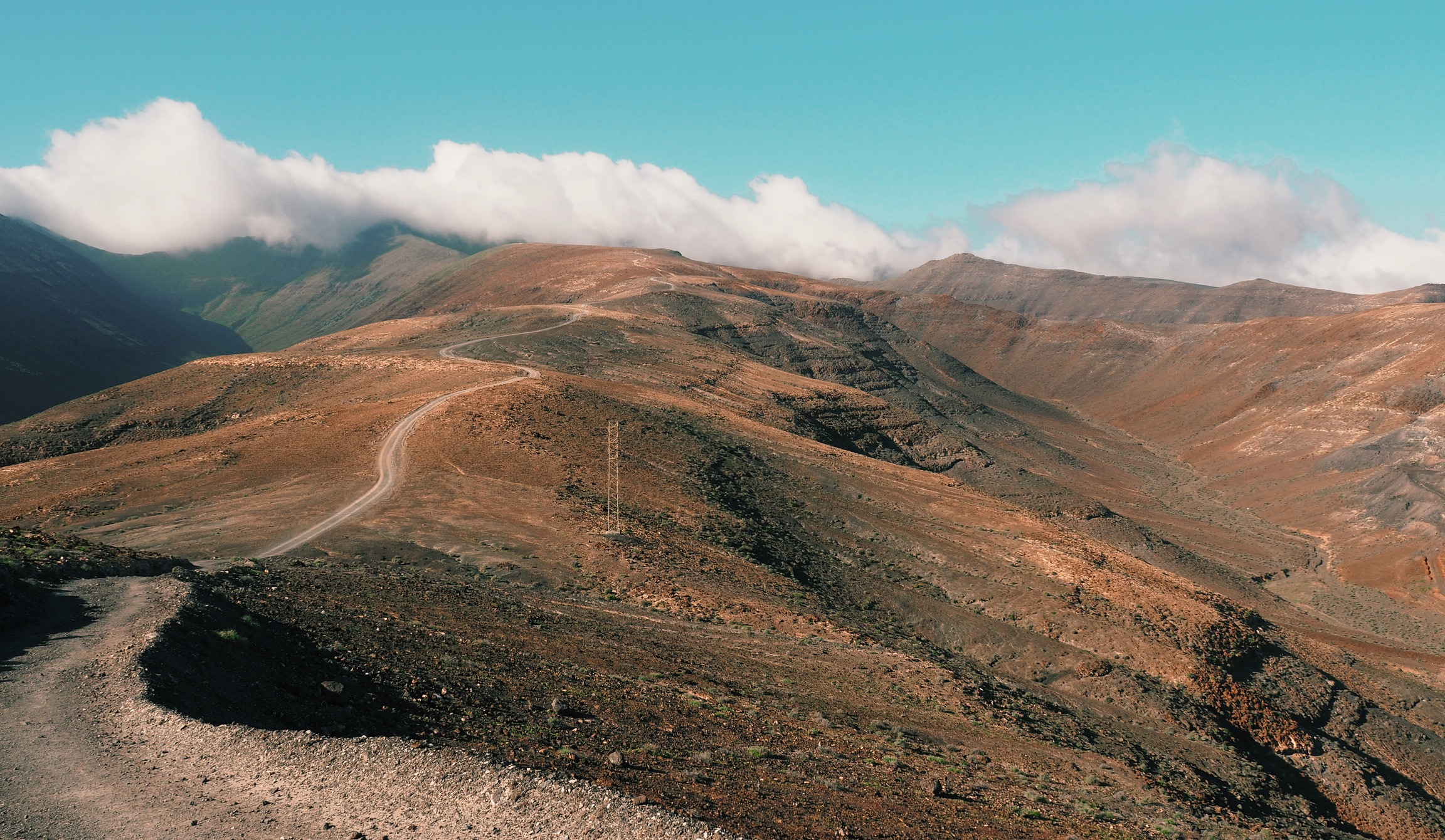 Long, winded hiking route along hill scenery with clouds over the top of Pico de La Zarza, Fuerteventura