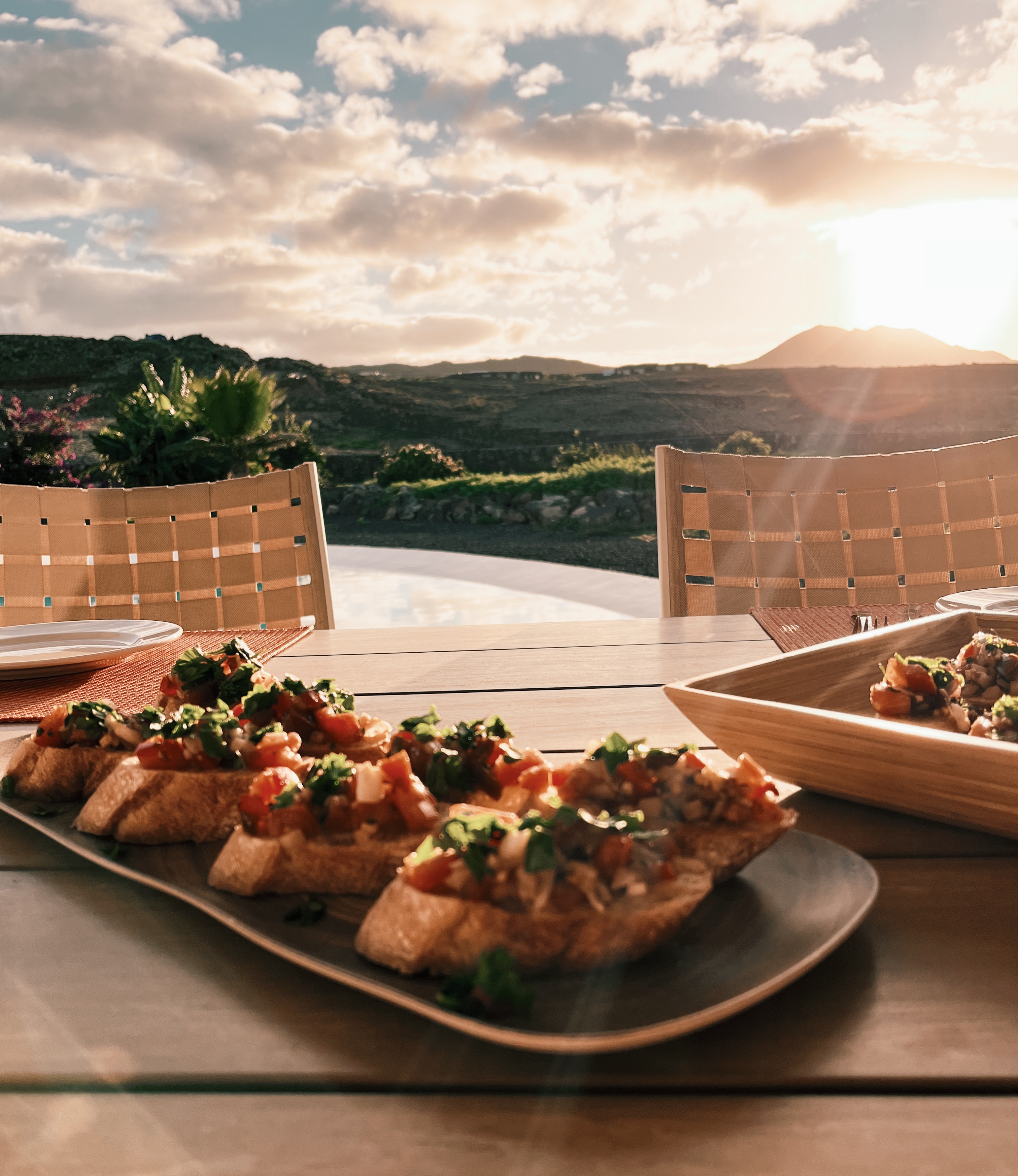 Bruschetta on large plate on a wooden table in front of sun setting over a small mountain in the distance on Fuerteventura, Spain